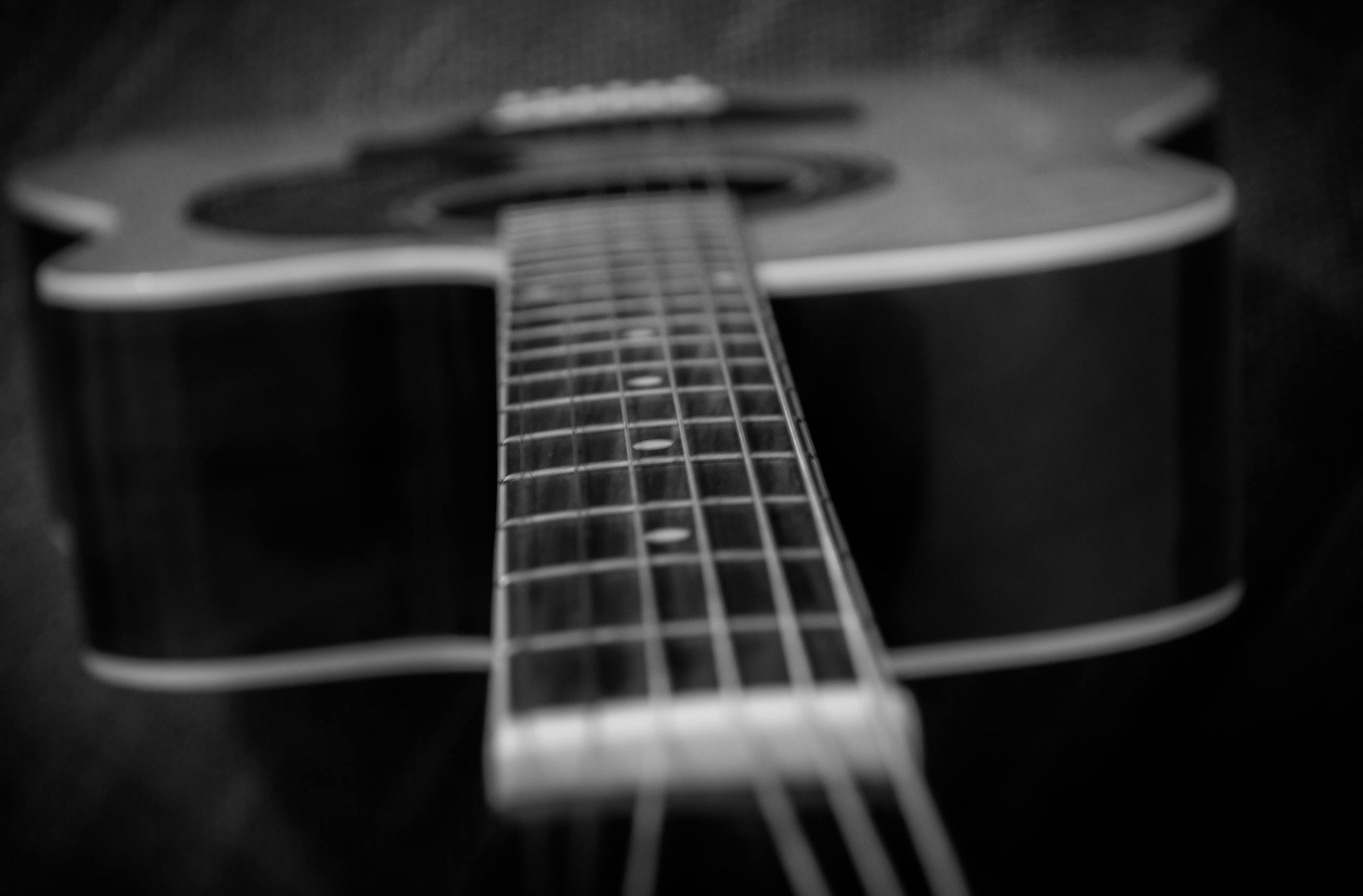 Artistic black and white close-up of an acoustic guitar neck, highlighting the strings and frets.